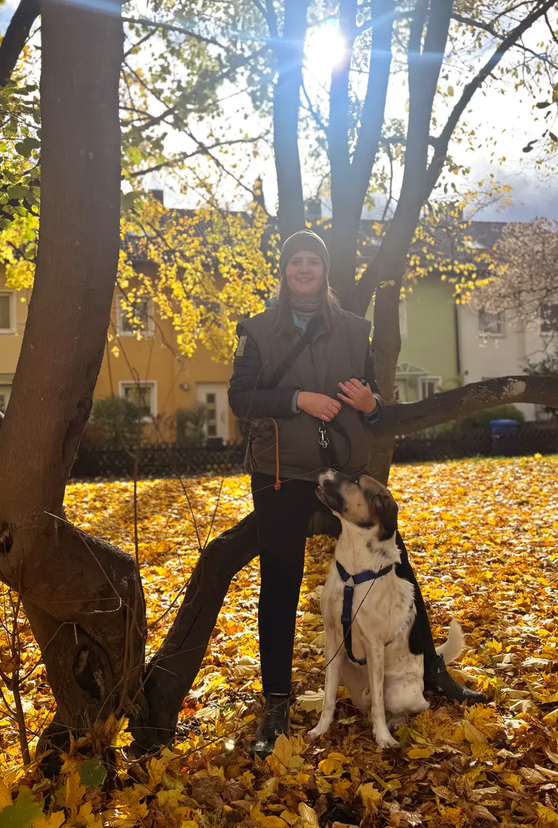 Veronique mit ihrem Hund unter einem Baum im goldenen Herbstlaub